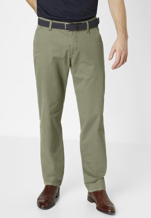 Khakifarbene Chinos mit geradem Schnitt, aus Baumwolle gefertigt, mit strukturierter Oberfläche und einem marineblauen gewebten Gürtel mit einer silbernen Schnalle. Braune Lederstiefel.