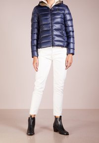 Giacca a vento navy con design a righe orizzontali, cerniera frontale e cappuccio. Abbinata a pantaloni bianchi e stivali neri alla caviglia. Texture morbida.