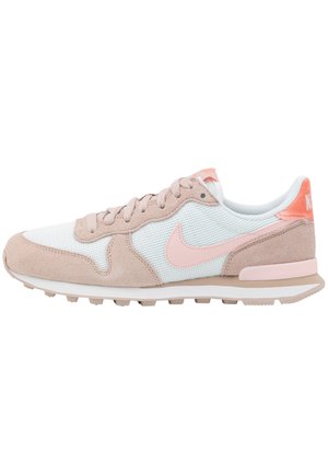 Jasnoróżowy i beżowy sneaker Nike z panelami z siateczki i zamszu, sznurowany z przodu, z fakturowaną podeszwą, widoczny z boku na białym tle.