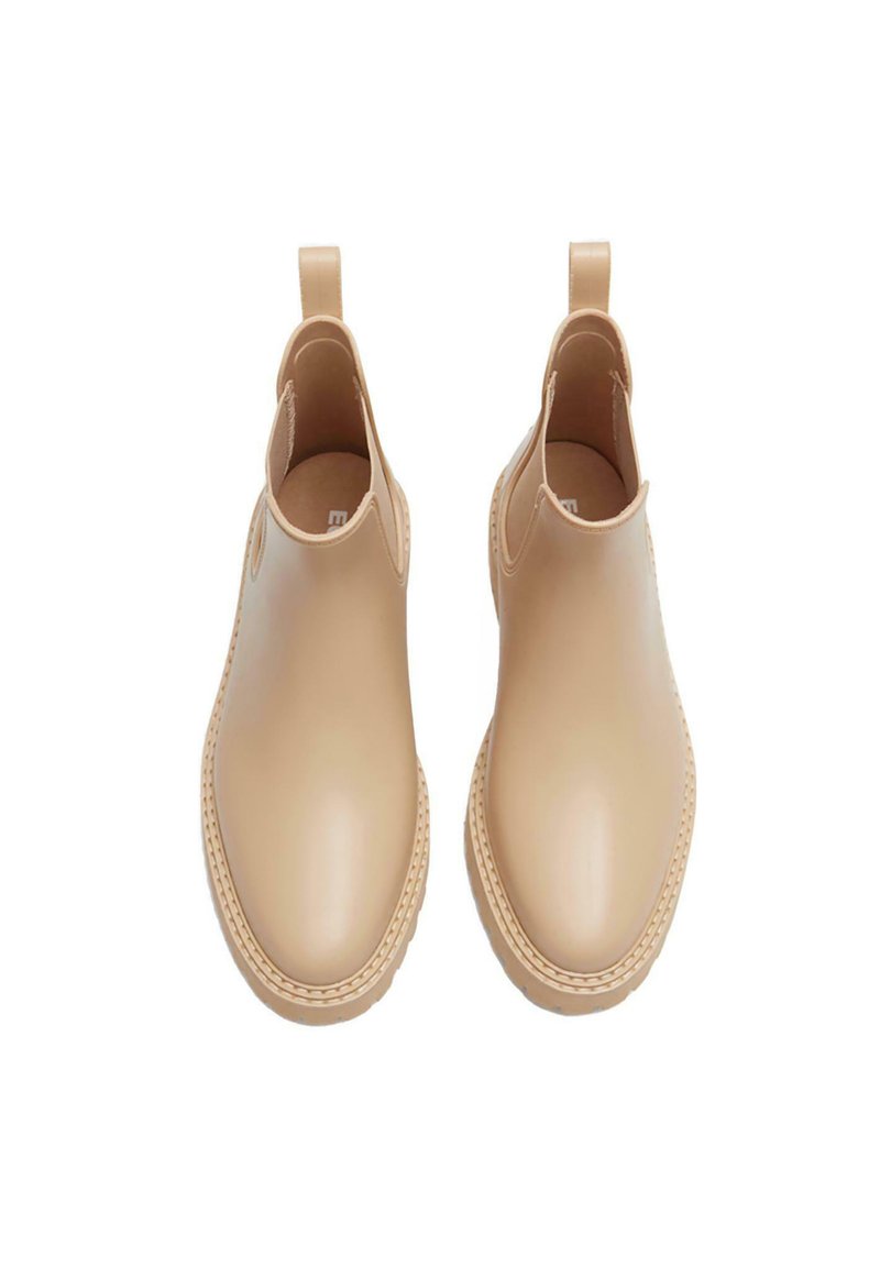 Botas de tobillo impermeables beige con un acabado liso, paneles laterales elásticos y lengüetas para facilitar el calzado. Suela texturizada para mayor agarre.