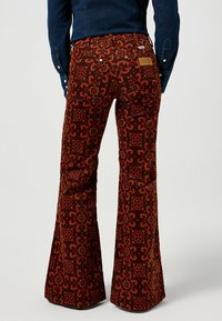 Uppvikta corduroybyxor i en rik rost-röd färg med ett detaljerat geometriskt mönster. Har två bakfickor och en märkesläderlapp.