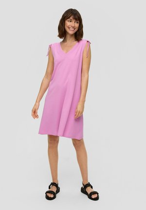 Rosa ärmelloses Kleid mit V-Ausschnitt, ausgestattet mit Bindeträgern an den Schultern und einer A-Linie, gefertigt aus einem glatten Stoff. Schwarze Plateausandalen.