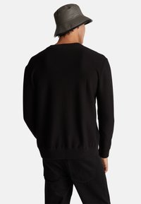 Maglione nero lavorato a maglia con maniche lunghe, collo rotondo e orlo a coste. Indossato con un cappello a secchiello grigio e pantaloni neri. Design minimalista.