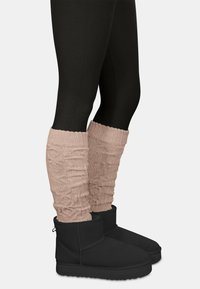 Schwarze Knöchelstiefel mit strukturiertem Design, kombiniert mit hellrosa gestrickten Stulpen mit gerafftem Muster.