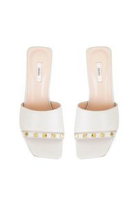 Sandales à glissière en cuir blanc avec un bout carré, une large sangle et des clous pyramides dorés le long de la bande. Texture lisse avec une semelle intérieure légère.