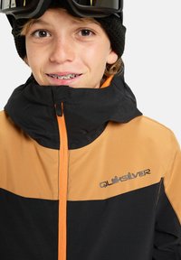 Black and orange ski jacket with a zip closure and high collar. Features Quiksilver logo on the chest in gray. Textured fabric.
