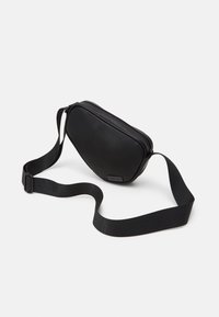 Black crossbody bag with a smooth, rounded design, textured zip closure, and adjustable strap, featuring a minimalist aesthetic.