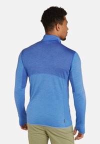 Jersey azul de manga larga con cuello alto, paneles texturizados y diseño sin costuras. Presenta tonos de azul contrastantes y costuras finas.