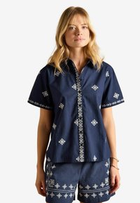 Cămașă bleumarin cu mânecă scurtă, brodată cu flori albe, cu nasturi în față și pantaloni scurți asortați cu motive similare. Material din amestec de bumbac.