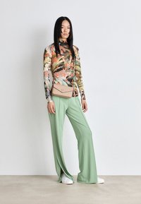 Dlouhý rukáv s barevným potiskem džungle, doplněný širokými mentolově zelenými kalhotami a béžovou crossbody taškou. Hladká, lehká tkanina.
