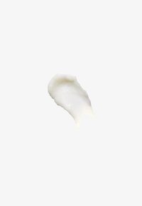 Produit cosmétique blanc crémeux avec une texture lisse, façonné en une petite touffe incurvée, sur un fond blanc uni.
