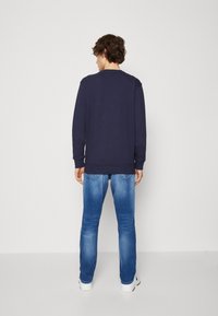 Sudadera de manga larga azul marino con cuello redondo, combinada con jeans de tiro bajo y lavado claro. El material parece suave con puños y dobladillo acanalados.