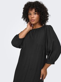 Musta mekko, joka on valmistettu kevyestä kankaasta, ja siinä on väljä istuvuus, puffy-hihat ja kerätyt hihansuut. Sileä tekstuuri, jossa hienovarainen laskos.