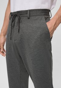 Graue sportliche Jogger mit einem Kordelzugbund, seitlichen Taschen, weichem Material und einem lockeren Schnitt, der ein glattes, meliertes Muster zeigt.