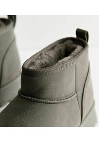 Las botas de tobillo de ante gris presentan un suave forro de piel de pelo y un puño texturizado, con un detalle de costura elevada alrededor de la suela.