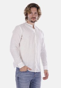 Camicia bianca in lino con colletto alla cinese, maniche lunghe e finitura testurizzata, abbinata a jeans in denim azzurro chiaro.