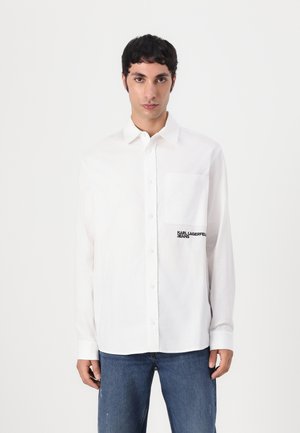Balta mygtukinė marška su krūtinės kišenėle, dekoruota juodu siuvinėjimu "KARL LAGERFELD JEANS". Medžiaga atrodo lygi ir lengva.