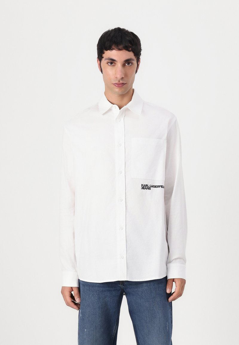 White button-up shirt with a chest pocket, featuring black "KARL LAGERFELD JEANS" embroidery. Fabric appears smooth and lightweight.