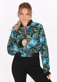 Korte bomberjack met een levendige tropische bladerenprint in tinten blauw en groen, voorzien van gouden kettingaccenten en zwarte ribgebreide afwerking.