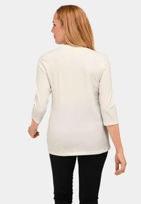 Cremefarbenes, semi-tailliertes Shirt mit Dreiviertelärmeln, glatter Textur und rundem Halsausschnitt, von hinten betrachtet.