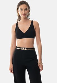Mustat raidoitetut bralette-topit, joissa on syvä V-kaula-aukko, yhdistettynä korkeavyötäröisiin mustiin housuihin, joissa on kultasävytteinen korostevyö.