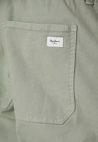 Svijetlozeleni tkaninski džep s izvezenom etiketom na kojoj piše "Pepe Jeans" i "LONDON" tamnim tekstom. Teksturirani, izdržljivi materijal.