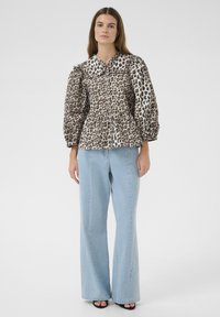 Leopardimustriga peplum-särgil on valge krae, puffvarrukad ja nööpide detail, mis on kokku sobitatud helesiniste laia säärega teksadega. Sile tekstuur.