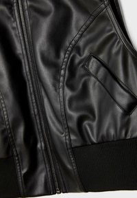 Część czarnej skórzanej kurtki pokazująca zamek błyskawiczny, skośną kieszeń i ściągacz z prążkowanej tkaniny na dolnym brzegu.