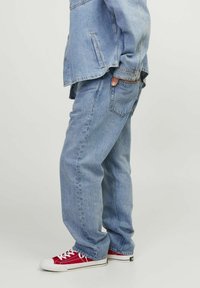 Jeans de denim albastre deschis cu o croială lejeră, picioare drepte și ușoare efecte de decolorare; asortați cu adidași roșii cu șireturi albe și vârfuri din cauciuc.