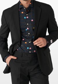 Zwarte blazer over een patroonshirt met blauwe maze-lijnen en kleurrijke pixelachtige geesten op een zwarte achtergrond, met contrasterende manchetten.