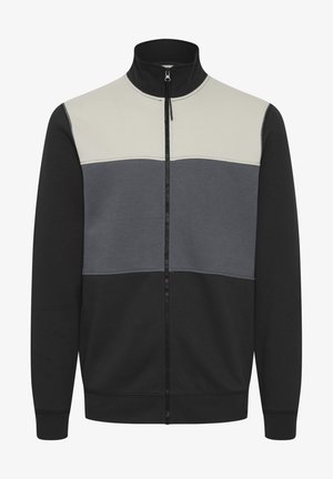 Zip-jacka med hög krage och design i vitt, grått och svart färgblock. Tillverkad av ett mjukt, stretchigt material.