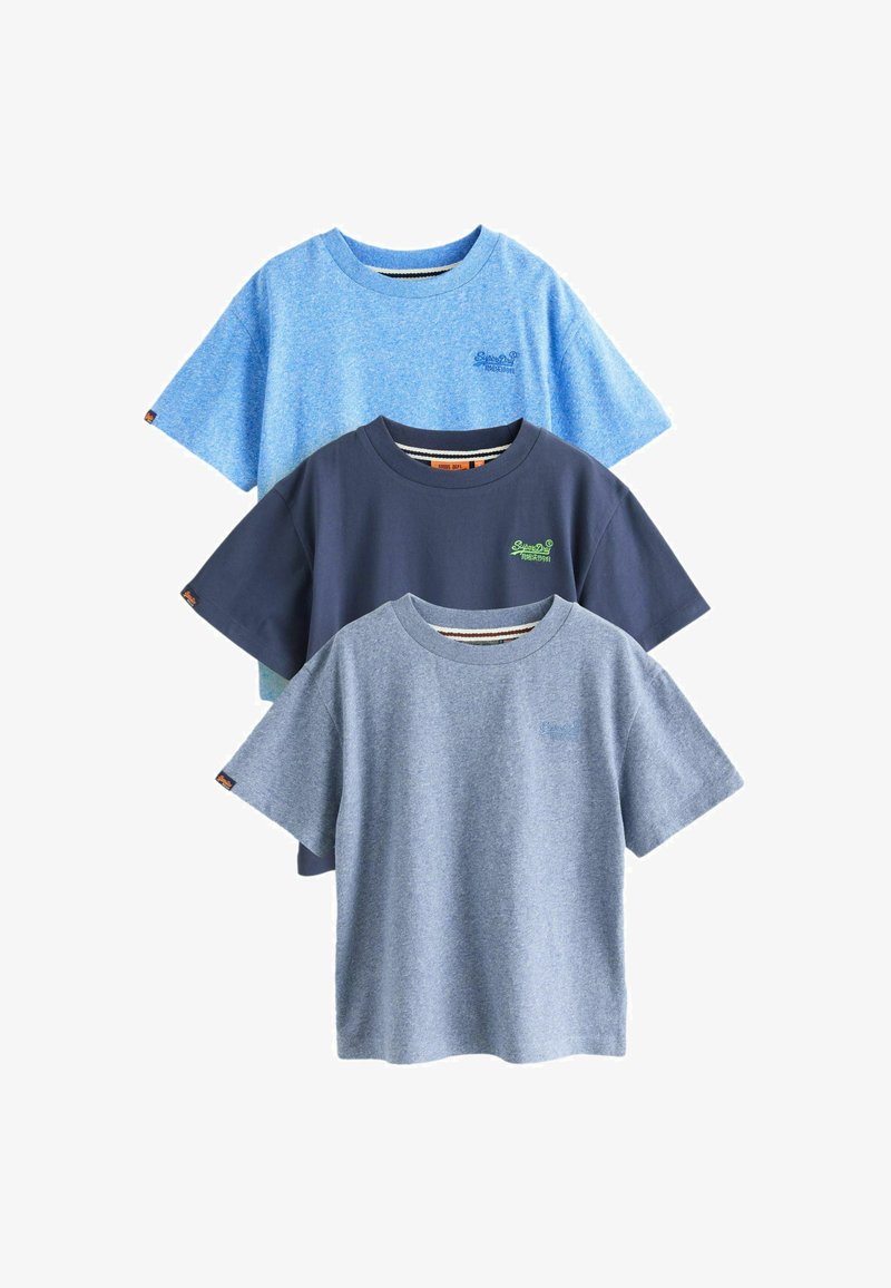Trois t-shirts à manches courtes et col rond dans des nuances de bleu, chacun avec une petite broderie de logo sur la poitrine gauche et une étiquette sur la manche gauche.