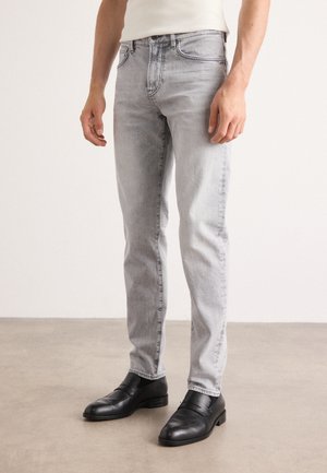 Light gray denim jeans, slim fit, featuring subtle whiskering. Paired with black leather shoes, showcasing clean lines and minimal detailing.