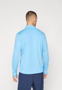 Langærmet, lyseblå polo-shirt med krave, der har glat stof og tætsiddende ærmer, set fra ryggen.
