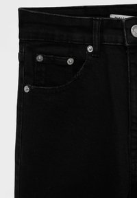 Gros plan sur un jean en denim noir montrant la poche avant avec rivets, passants de ceinture et fermeture à bouton métallique sur la ceinture.