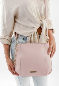 Borsa a tracolla rosa in pelle con finitura testurizzata, accessori in oro e dettaglio a catena attaccato a una tracolla.