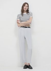 T-shirt a righe cropped in bianco e nero, abbinato a pantaloni grigi a vita alta e a gamba larga. Scarpe in pelle nere con suola piatta.