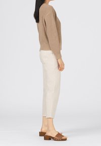 Beżowy sweter dziany o luźnym kroju, kremowe spodnie i brązowe klapki na drewnianym obcasie. Prosty, teksturowany wzór, widok z boku.