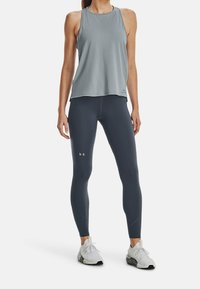 Top atletico senza maniche grigio abbinato a leggings grigi scuri. L'outfit presenta una texture liscia e accenti di logo sia sul top che sui leggings.