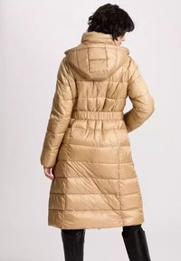 Beżowa kurtka puchowa z kapturem, z pikowanym wzorem, paskiem w talii, długimi rękawami i średniej długości krojem. Gładka, błyszcząca tekstura.