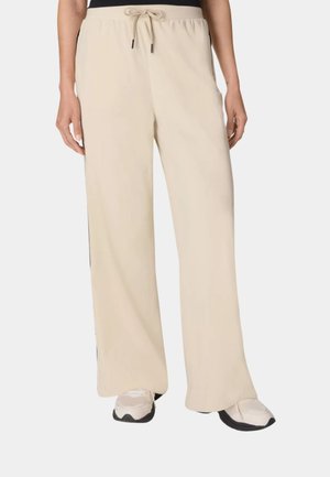 Beige wijde broek met aantrekkoord in de taille, gedragen met witte en zwarte sneakers, getoond op een persoon van taille tot voeten.