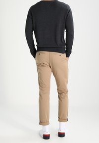 Pull gris foncé, chinos couleur sable avec revers retroussés, chaussures blanches avec accents rouges et bleus, vues de dos sur un fond uni.