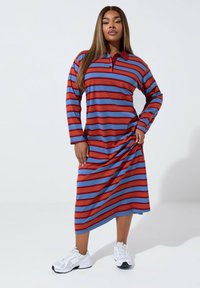 Czerwona i niebieska w paski, długa sukienka z długim rękawem, z kołnierzykiem i asymetrycznym dołem. Połączona z białymi sportowymi trampkami.