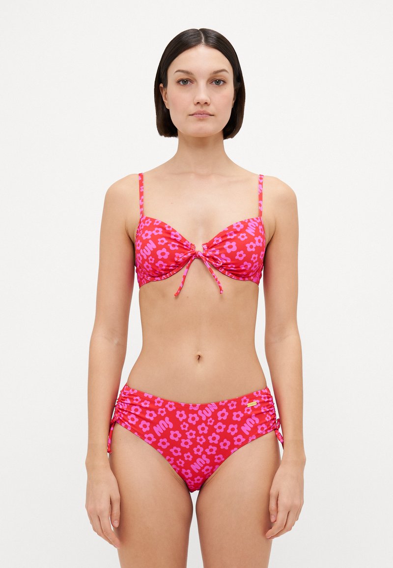 Conjunto de bikini em rosa com padrões florais. O top apresenta um laço no centro e alças ajustáveis; as calças têm franzidos laterais com detalhes decorativos.