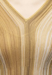 Gros plan d'un tissu tricoté à rayures or et beige formant un décolleté en V sur un vêtement.