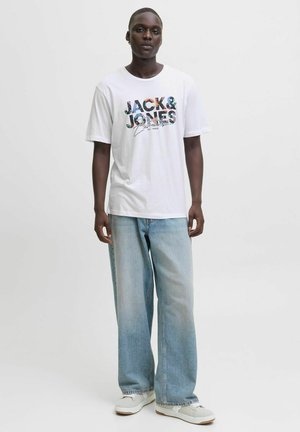 Hvid kortærmet t-shirt med farverig "JACK & JONES" grafik på forsiden, parret med lyseblå vidde bukser og hvide sneakers.