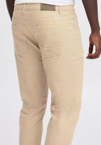 Pantaloni in cotone beige con vestibilità dritta, tasche posteriori con una sottile cucitura a zigzag e un'etichetta in pelle sulla vita.