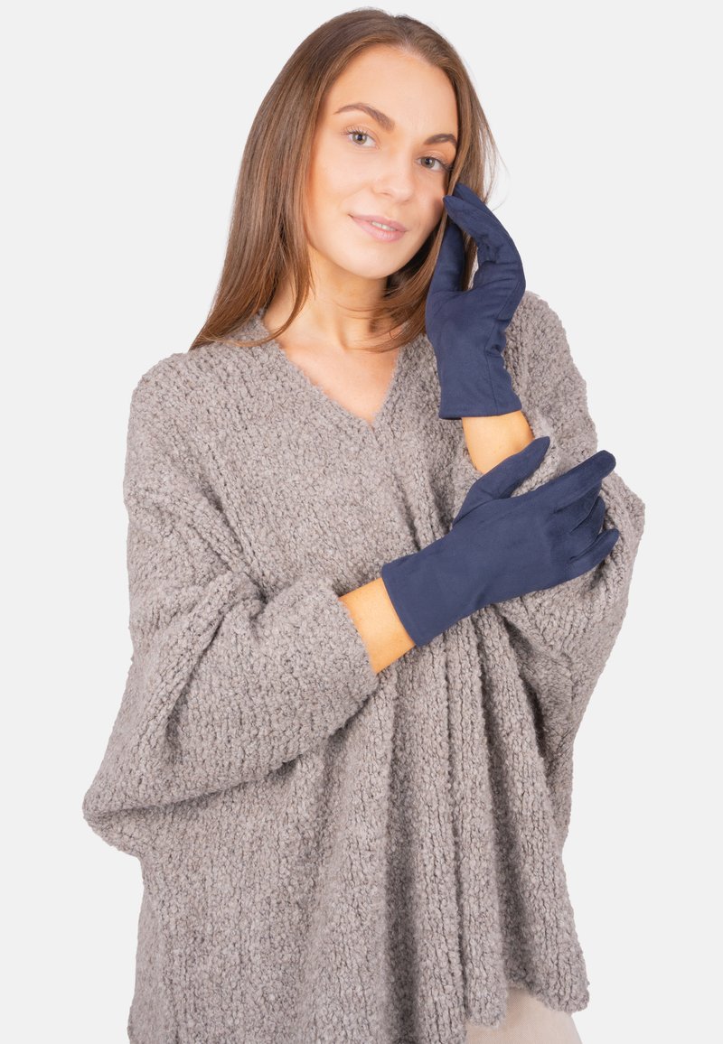 Marineblaue Handschuhe aus glattem Material, taillierte Form mit langen Bündchen, kombiniert mit einem strukturierten grauen Pullover.