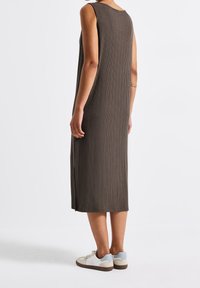 Sukienka bez rękawów w kolorze oliwkowym z bocznymi rozcięciami. Posiada okrągły dekolt i zestawiona jest z białymi sneakersami z jasnoniebieskimi akcentami.