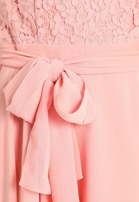 Růžový šaty s krajkovou korzetou, splývavou šifonovou sukní a velkou mašlí v pase. Hladká textura a měkká, lehká látka.